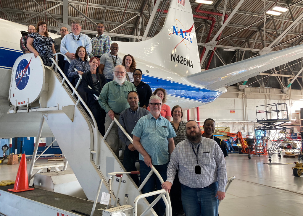 Members of the Engineering and Technology Directorate standing on the stairs of a NASA labeled plane.