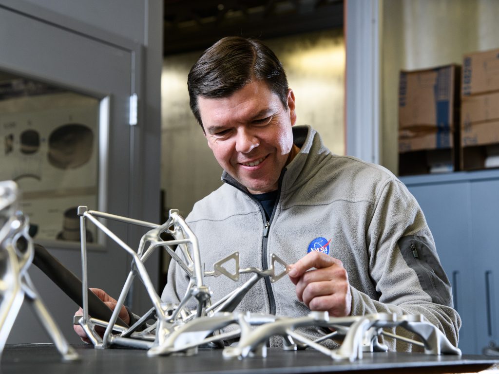 NASA Engineer Ryan McClelland, Code 550, examines structures designed by an AI for various missions. Most products are milled out of solid blocks of aluminum though others have been produced by 3D printing titanium. Credit: NASA/Denny Henry