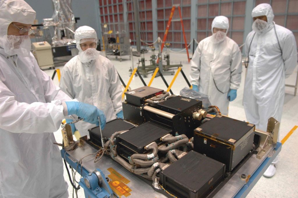 Four engineers in a clean room working on the Hubble Space Telescope.