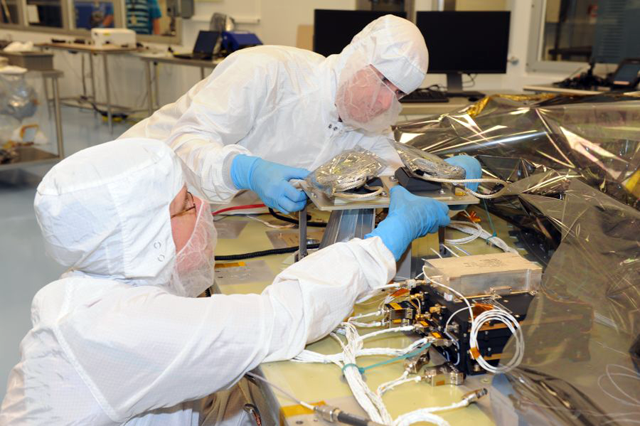 Two engineers working on installing an instrument onto a space deck in a clean room.