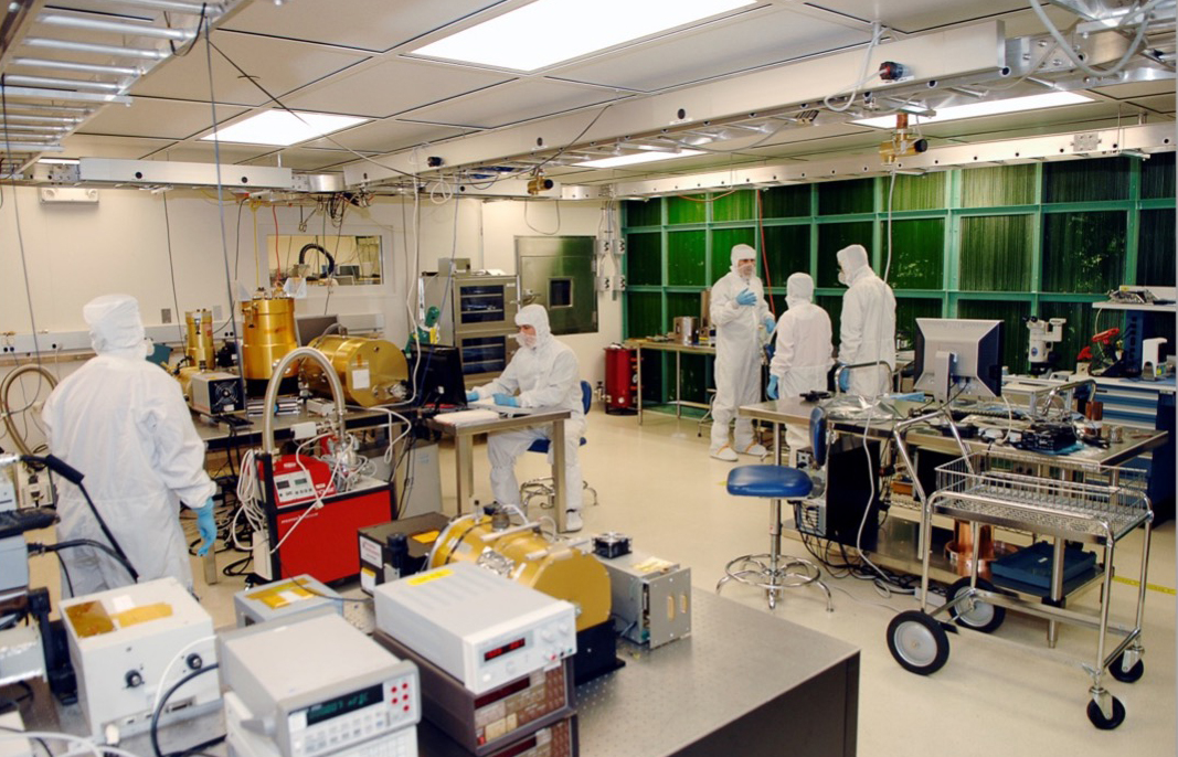 Five engineers in white coveralls called "bunny suits" working in the Detector Characterization Laboratory for testing of detectors for flight and technology developments