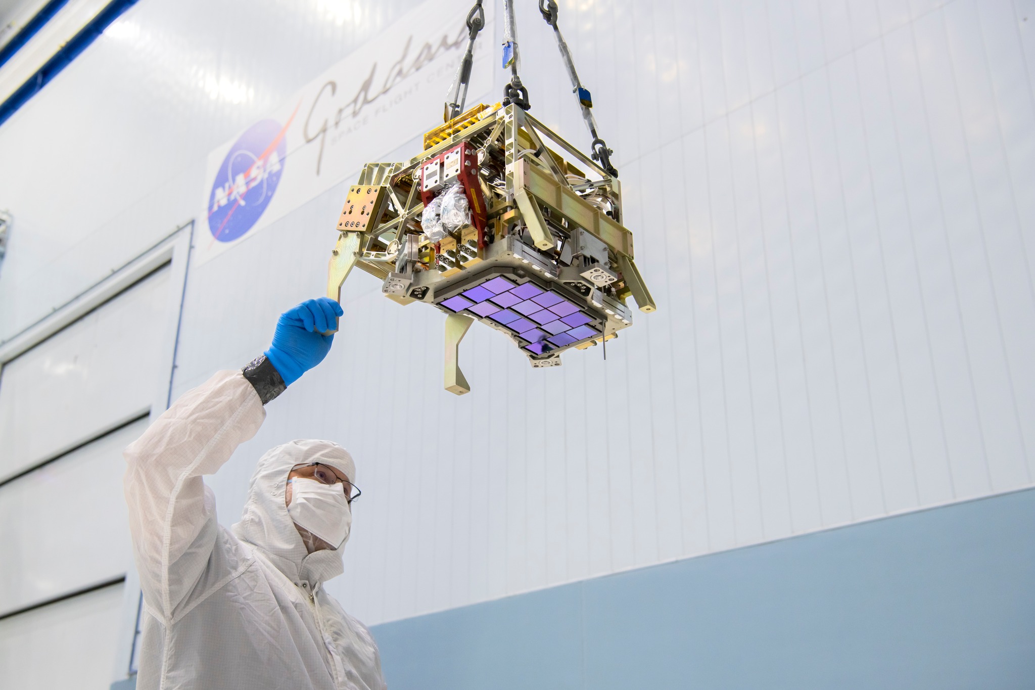 In this photo, an engineer inspects the Roman Space Telescope’s Focal Plane System (FPS), suspended from a crane in NASA GSFC’s Spacecraft Systems Development and Integration Facility. The FPS contains 18 detectors that form a Mosaic plate.