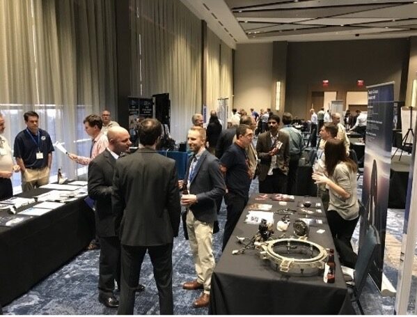 In this photo, engineers gather at American and European Mechanism Symposia to exchange technology developments and lessons learned in the fields of precision mechanisms and space tribology through presentations and booth exhibits